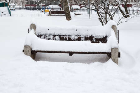 Snow covered bench among snowbanks in city parkの写真素材