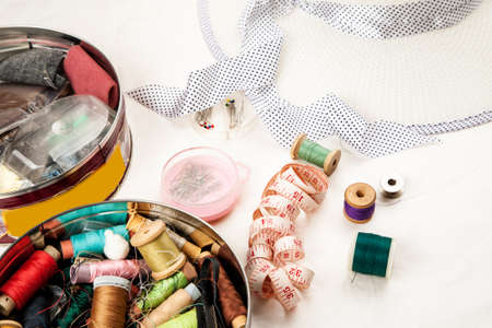 Set of tools and accessories for sewing and needlework with threads in spools, needles, measuring tape and other items on a white backgroundの写真素材