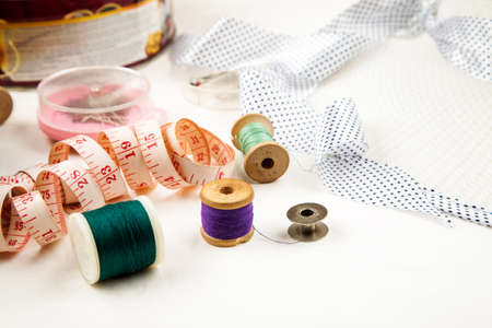Set of tools and accessories for sewing and needlework with threads in spools, needles, measuring tape and other items on a white backgroundの写真素材