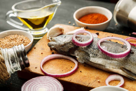 Fresh fish with herbs and spices on vintage cutting board on dark backgroundの写真素材