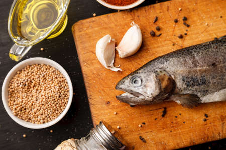 Fresh fish with herbs and spices on vintage cutting board on dark backgroundの写真素材