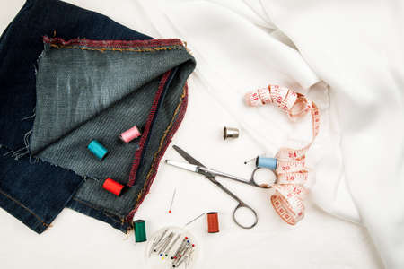 Set of tools and accessories for sewing and needlework with threads in spools, needles, measuring tape and other items on a white backgroundの写真素材