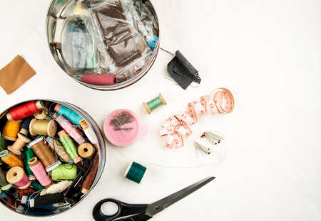 Set of tools and accessories for sewing and needlework with threads in spools, needles, measuring tape and other items on a white backgroundの写真素材