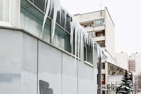 Long sharp icicles on a roof of a gray buildingの写真素材