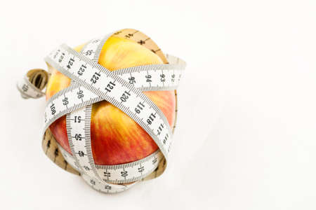 Ripe red juicy apple with measuring tape around it on a white backgroundの写真素材