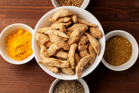 Raw dry soya meat chunks in a white bowl on a wooden table with different species, top viewの写真素材