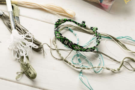 Friendship bracelets with threads on a white wooden table, top viewの写真素材