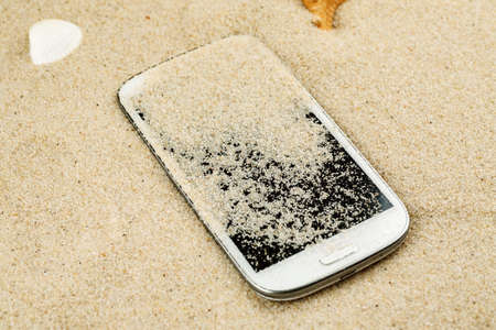 White smartphone lost in sand on the beachの写真素材