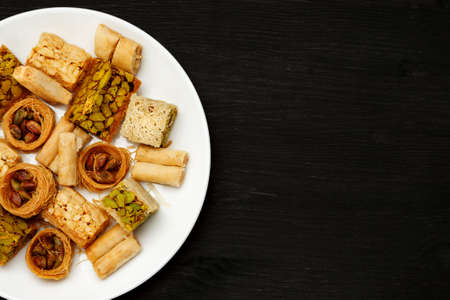 Traditional oriental sweets in white plate with different nuts on a black table, top view, copy...