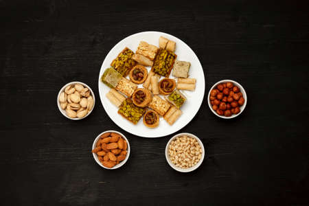 Traditional oriental sweets in white plate with different nuts on a black table, top viewの写真素材