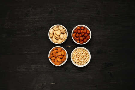 Different nuts in ceramic bowls on a black wooden table, top vievの写真素材