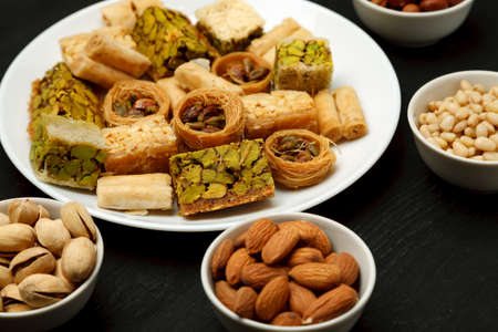Traditional oriental sweets in white plate with different nuts on a black table, close-up shotの写真素材