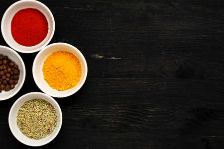 Different spices in ceramic bowls on a black wooden table, top view, text spaceの写真素材