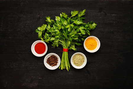 Bunch of green fresh parsley with spices in white ceramic bowls on a black wooden table, top viewの写真素材