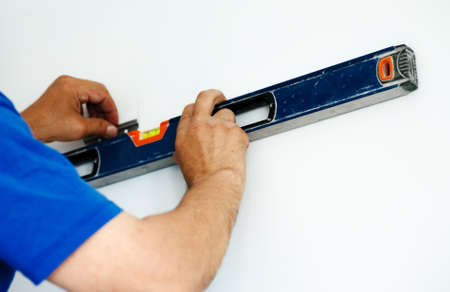 Hands of worker with bubble level on white wall