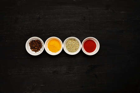 Different spices in ceramic bowls on a black wooden table, top viewの写真素材