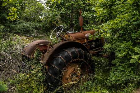 Old rusty tractor that stands among bushes with corase tires and snow chainsの写真素材