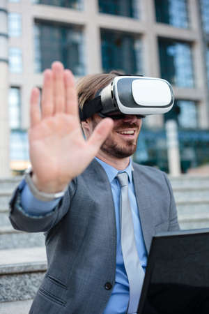 Close up of a young businessman using VR goggles in front of an office building. Selective focus concept, focus on head. Working with modern technologies conceptの写真素材