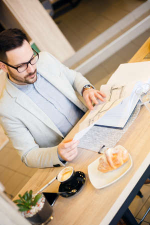 Young architect looking over building plans while working in a modern cafe. High angle view