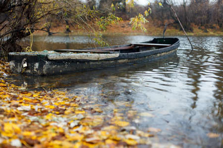 Old wooden rowing boat floating in water near shore on a rainy autumn day