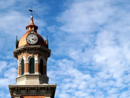 A brick and brass clock tower against a cloudy blue skyの写真素材