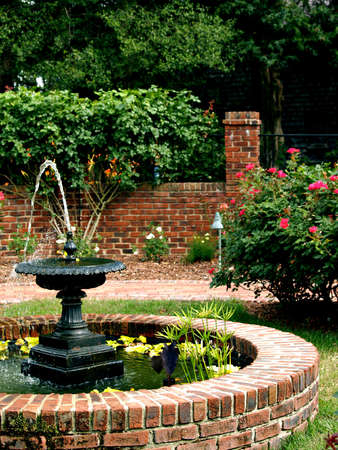 A water fountain sits in the middle of a pretty landscaped gardenの写真素材
