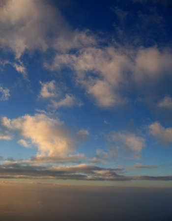 Puffy clouds with sunlight just starting to touch them in a pretty blue skyの写真素材