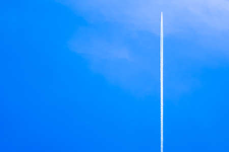 Airplane with contrail high in the blue skyの写真素材
