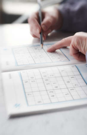 Woman trying to solve Sudoku Puzzle - window, sunlight, and coffee の写真素材