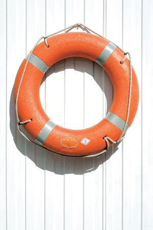 Orange lifebuoy on fence. A view of an orange lifebuoy or rescue device on a white fence.