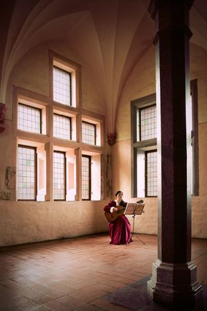 Woman playing guitar in castle.  A woman playing a guitar while sitting in a large open room in Marlbork Castle, Poland.の写真素材