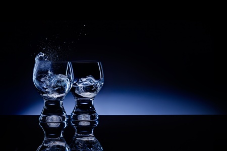 A picture of two shaped transparent shot glass with choppy liquid and ice.の写真素材