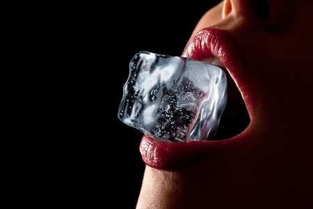 Ice cube in a woman's mouth against black background.