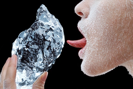 Side portrait of young woman with frozen face licking large block of ice, black background.の写真素材