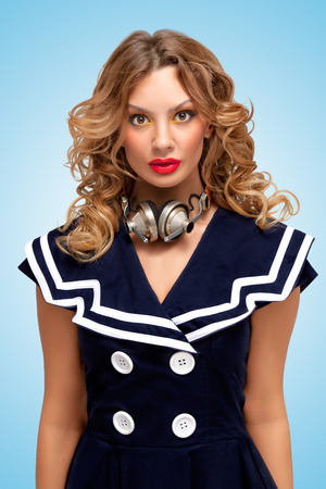 Retro photo of a fashionable pin-up sailor girl with metal vintage music headphones around her neck on blue background.の写真素材
