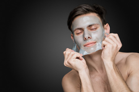 Portrait of a beautiful young man peeling off a facial mask, face and body skin care retreat.の写真素材