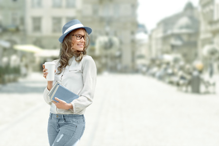 Happy young student with a coffee-to-go, holding books for reading and studying against urban city background.の写真素材