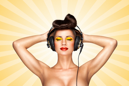 Retro photo of a nude pin-up girl with big vintage music headphones on colorful abstract cartoon style background.の写真素材