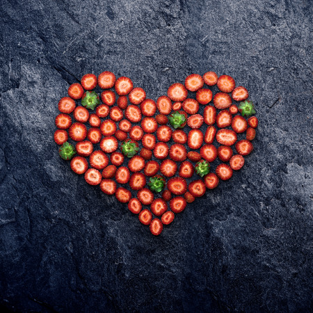 Valentine and love concept, creative still life of heart made of sliced strawberries, on stone background.の写真素材