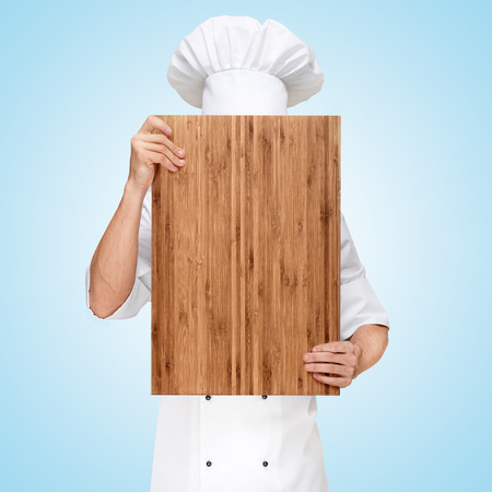 Restaurant chef hiding behind a wooden chopping board for a business lunch menu with prices.の写真素材