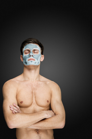 Portrait of a beautiful young man with a facial mud clay mask, face and body skin care treatment.の写真素材