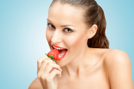A creative portrait of a beautiful girl biting a red ripe strawberry sexually.の写真素材
