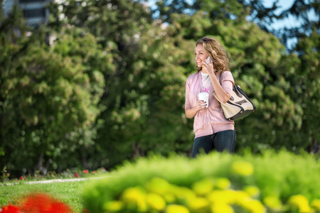 A beautiful woman with the phone holding a cup of take away coffee in a summer city.の写真素材