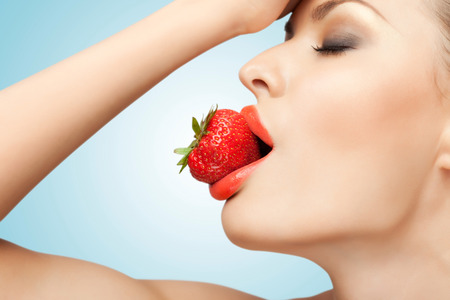 A portrait of a nude sexy woman holding a red-ripe strawberry in her mouth.の写真素材