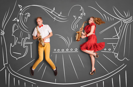 Love story concept of a romantic couple against chalk drawings background. Musician couple playing serenade on saxophone on stage.の写真素材