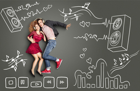 Happy valentines love story concept of a romantic couple sharing headphones and listening to the music against chalk drawings background of acoustic system, equalizer and player icons.の写真素材