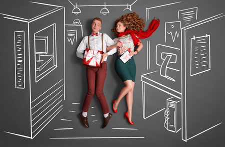 Happy valentines love story concept of an office romance. Young couple at work smiling at each other and sharing gifts against chalk drawings office background.の写真素材