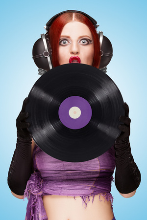 Colorful photo of a sexy emotional girl, wearing huge vintage music headphones and holding a purple LP microgroove vinyl record on blue background.の写真素材