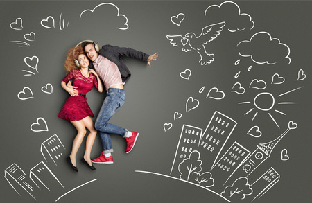 Happy valentines love story concept of a romantic couple sharing headphones and listening to the music against chalk drawings urban background.の写真素材