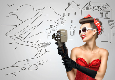 Glamorous pin-up tourist girl filming landscape with an old retro cinema 8 mm camera, standing on sketchy background.の写真素材